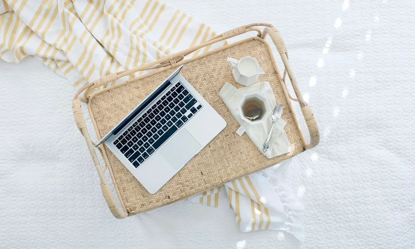 A laptop and coffee on a woven tray