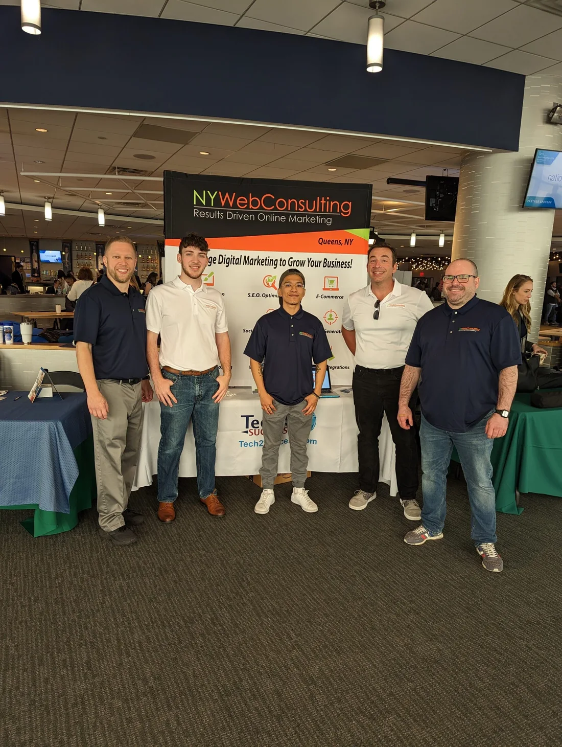 NY Web Consulting team members at an event beside the company display